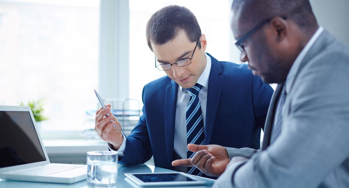 Image of two young businessmen discussing data in touchpad at meeting